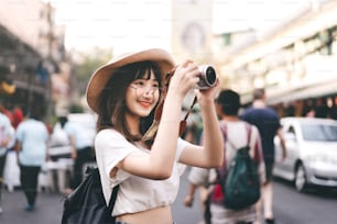 Young asian cute glasses girl hipster style traveller. Backpack solo local traveling take a photo with camera. Sightseeing at Khaosan road street market and food landmark. Bangkok, Thailand.