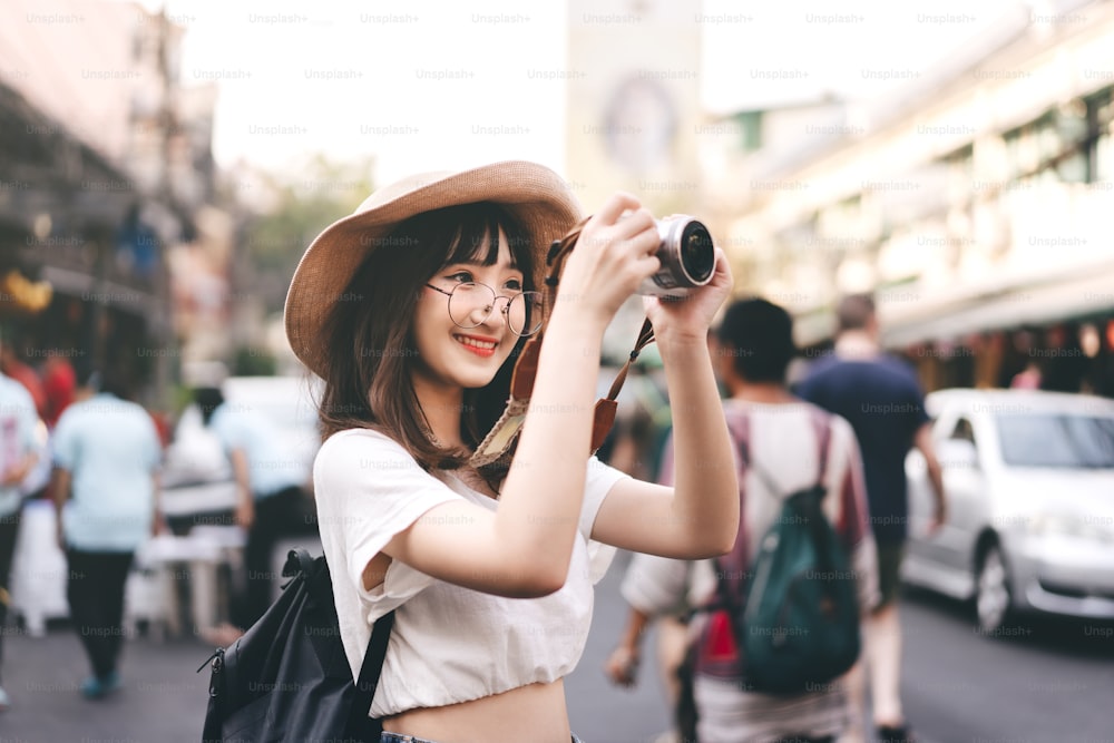 Jovem asiático óculos bonitos menina hipster estilo viajante. Mochila solo local viajando tirar uma foto com a câmera. Passeios turísticos no mercado de rua da estrada Khaosan e marco de alimentos. Banguecoque, Tailândia.