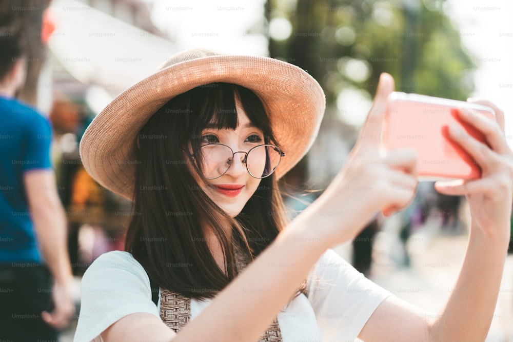 Jovens asiáticos óculos menina hipster estilo influência e viajante. Mochila solo local viajando com câmera de smartphone e upload para compartilhar rede social. Viagem com conceito de estilo de vida moderno.