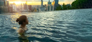 Silhouette noire de femme asiatique éclabousser de l’eau pendant les vacances d’été se détendre dans la piscine à débordement avec vue sur le coucher du soleil sur la mer bleue avec un paysage aérien urbain de grande hauteur au centre-ville Healthy happiness lifestyle