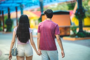 Young lovers couple hold hands, dating at amusement park, concept of happy, love, and relaxing