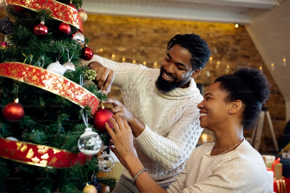 Happy African American couple enjoying while decorating Christmas tree together at home.