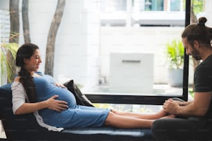 Mujer embarazada acostada en un sofá. Un hombre le masajea los pies. Ella está muy contenta y está bien, concepto de familia en casa