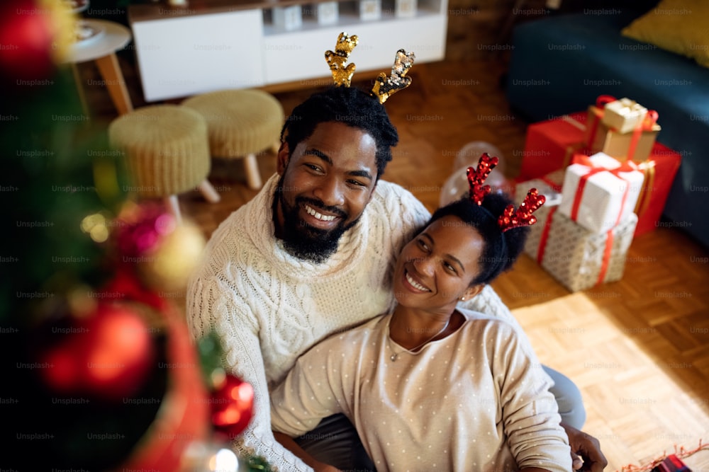 Happy African American couple relaxing by Christmas tree and enjoying in holidays at home.