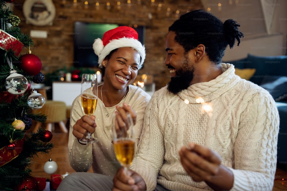 Mulher afro-americana alegre e seu marido se divertindo com espumantes e bebendo champanhe no Natal.
