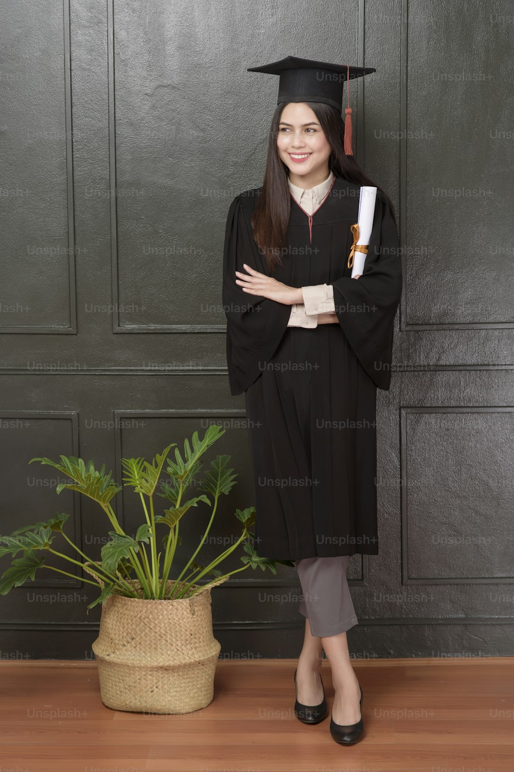Ritratto di giovane donna in abito da laurea che sorride e fa il tifo su sfondo nero