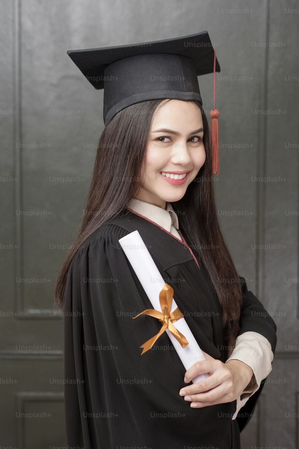 Portrait of young woman in graduation gown smiling and cheering on black background