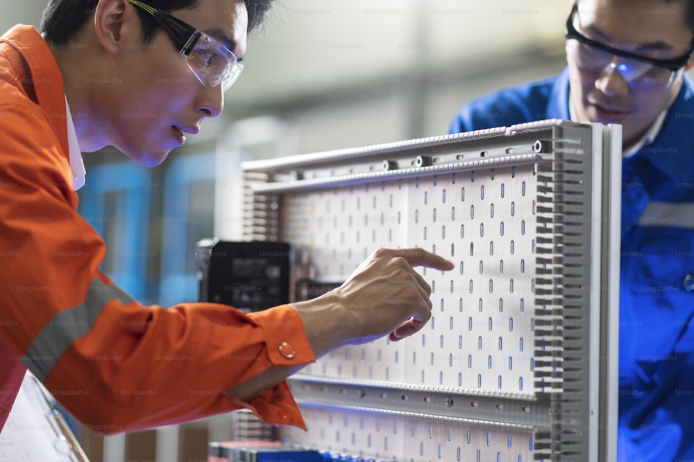 工場で機械のそばに立って議論をしているアジアの男性エンジニアの専門家、2人のアジア人の同僚が説明し、機械のプロセスcurcuitマザーボードを解決します