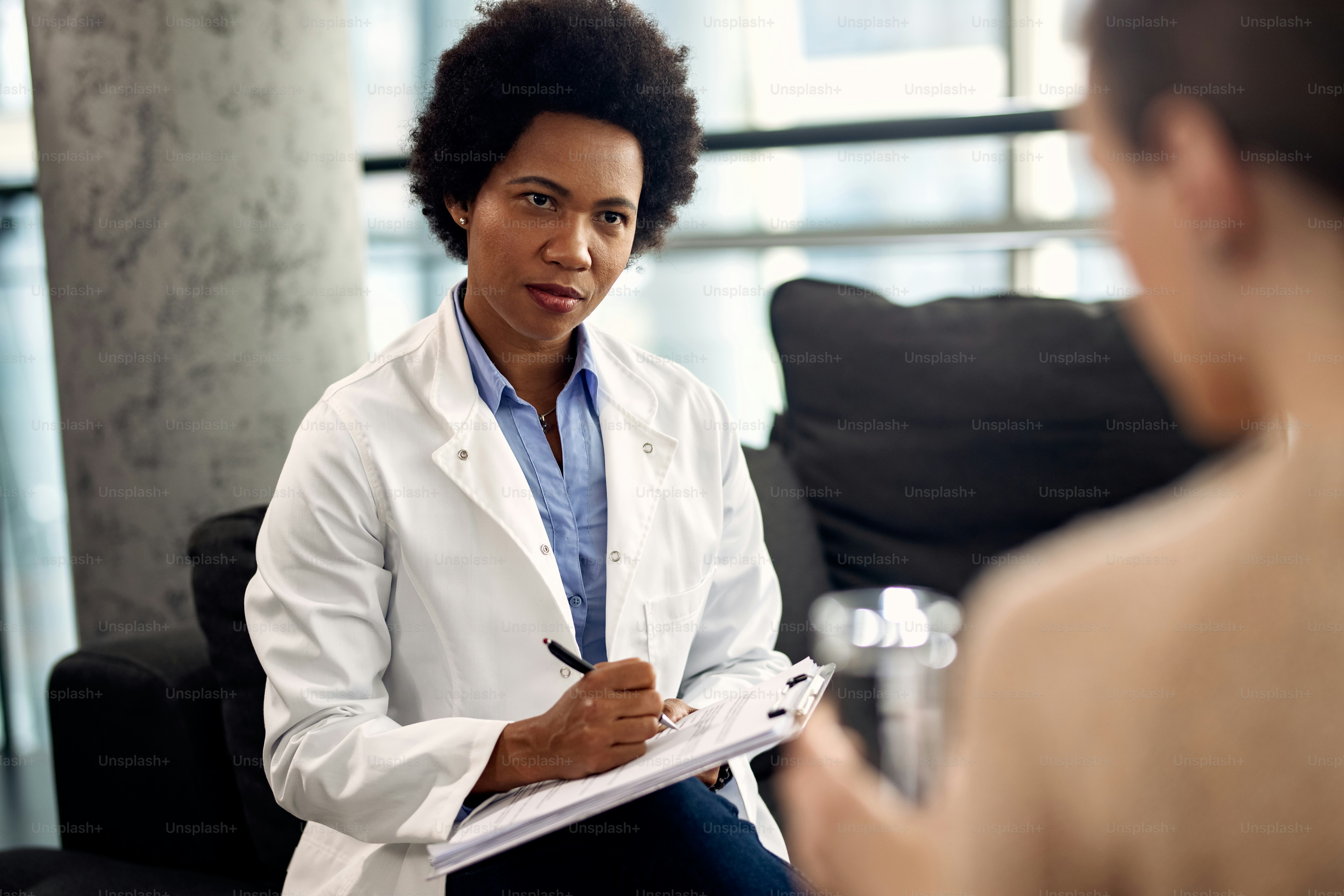 Un médecin afro-américain rédige des notes tout en écoutant un patient lors d’une séance de psychothérapie.
