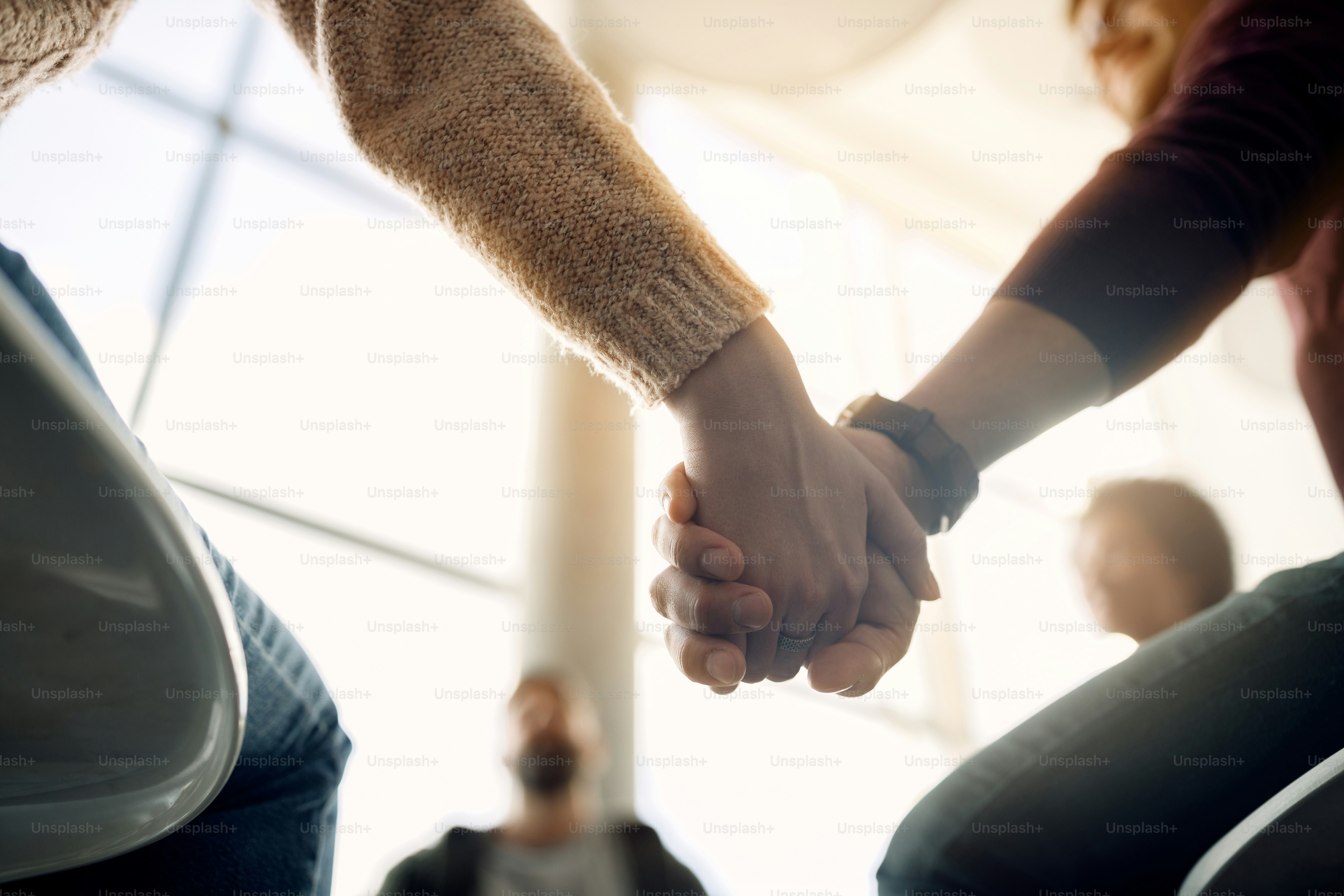 Gros plan sur les participants à la thérapie de groupe se tenant la main pendant la réunion.