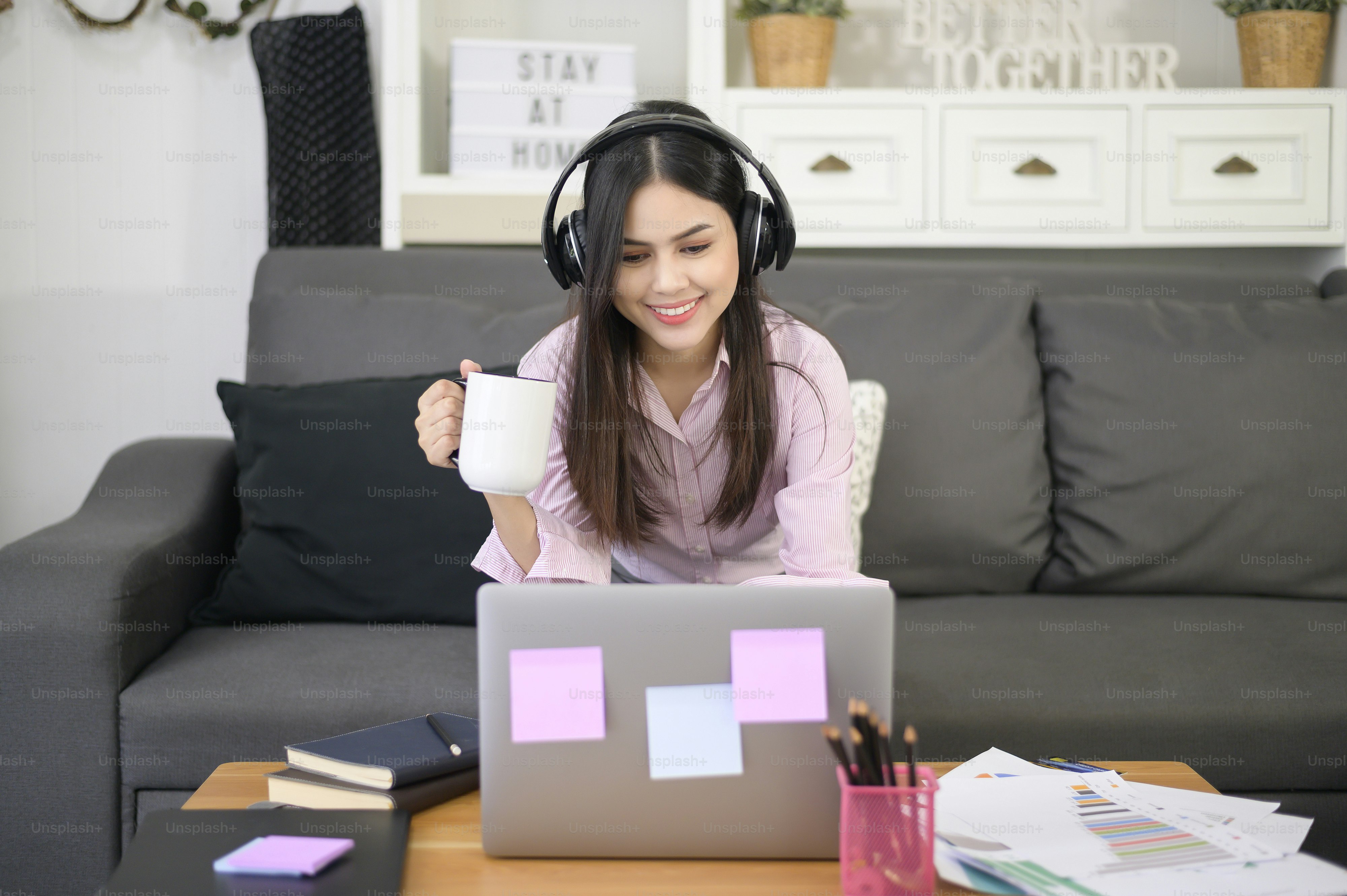 Seorang wanita muda cantik yang mengenakan headset sedang melakukan panggilan konferensi video melalui komputer di rumah, konsep teknologi bisnis.