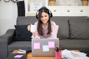A beautiful young woman wearing headset is making video conference call via computer at home , business technology concept .