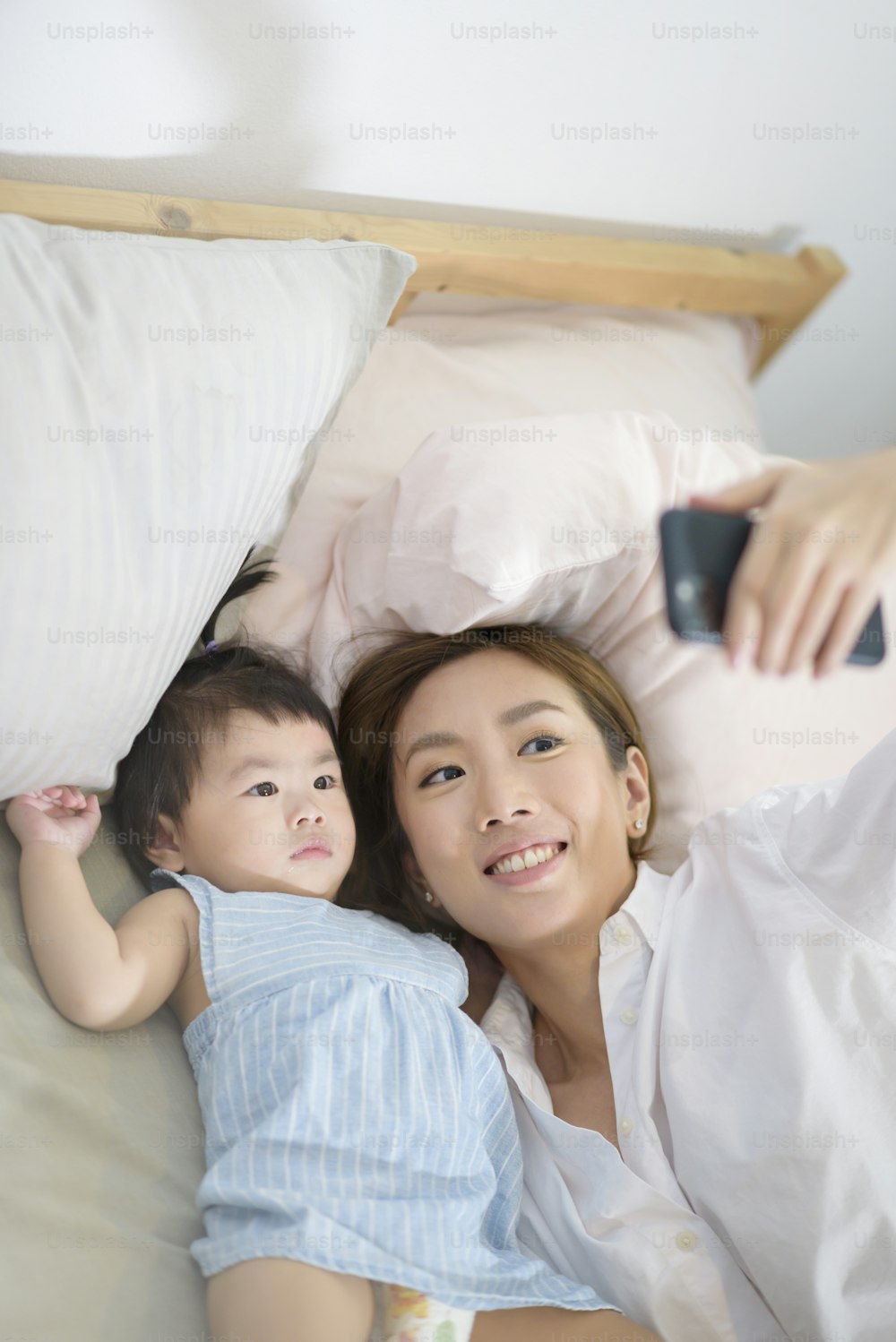 Asian Mother and her baby daughter are making selfie or video call to father in bed , Family , Home safety , parenthood , technology concept .
