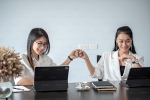 Dos jóvenes empresarias asiáticas chocan los puños y usan una tableta digital con sus colegas en la oficina.