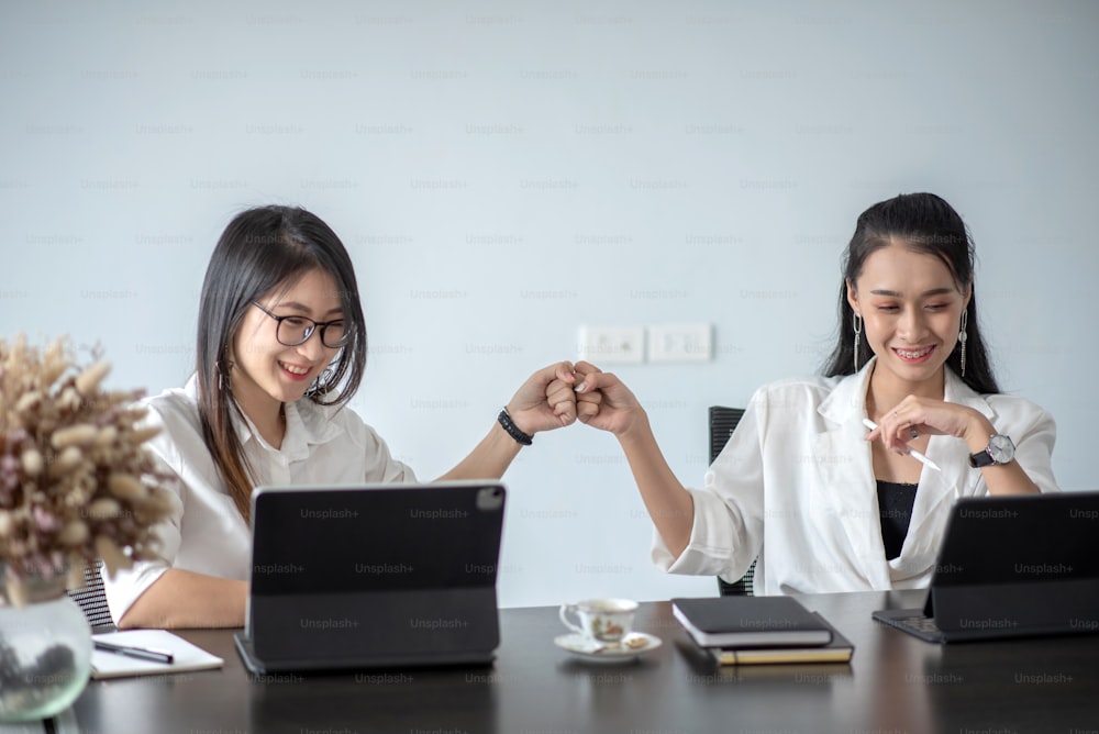Zwei junge asiatische Geschäftsfrau fist bump und nutzt digitales Tablet mit ihren Kollegen im Büro.