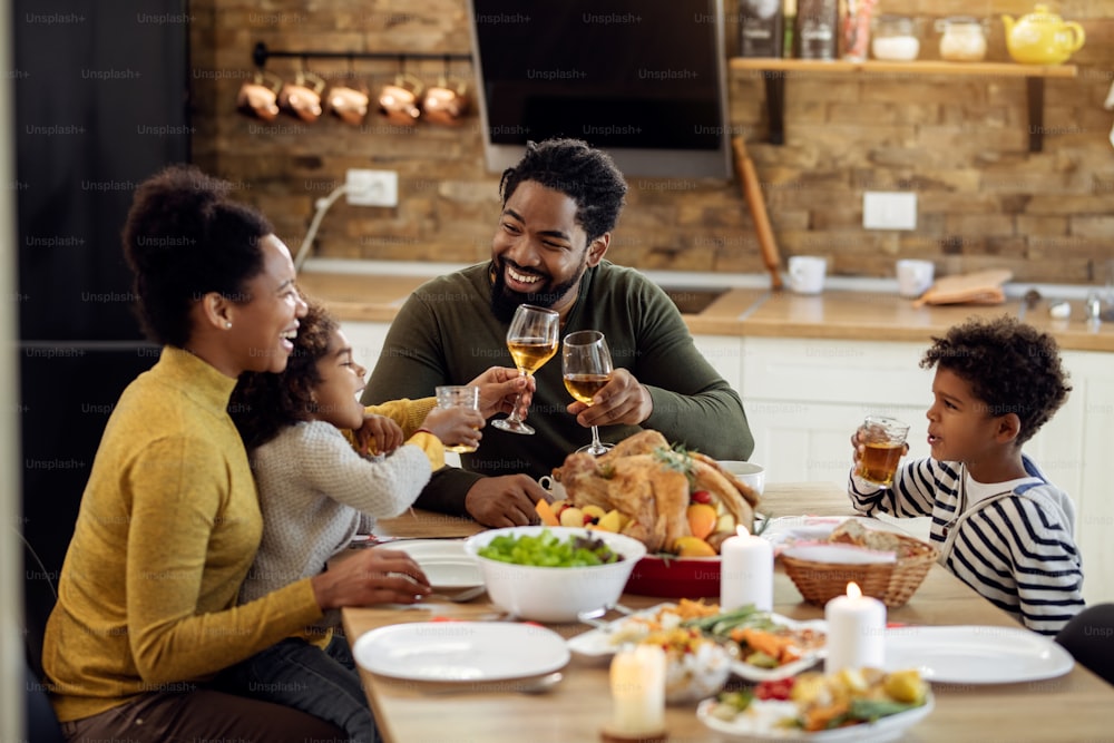 행복한 흑인 부모와 아이들은 식탁에서 가족 점심 식사 동안 추수 감사절을 축하하면서 건배합니다.