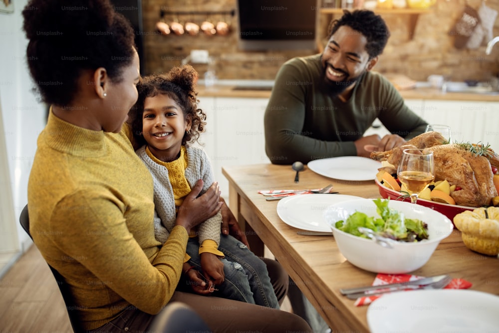 Feliz familia afroamericana disfrutando en el almuerzo de Acción de Gracias en la mesa del comedor. El enfoque está en una niña pequeña que mira a la cámara.