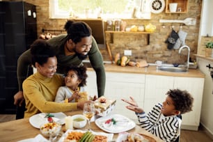 Happy black kids receiving Christmas presents form their parents during family lunch at home.