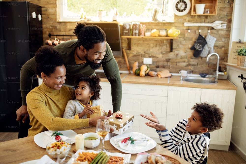 Happy black kids receiving Christmas presents form their parents during family lunch at home.