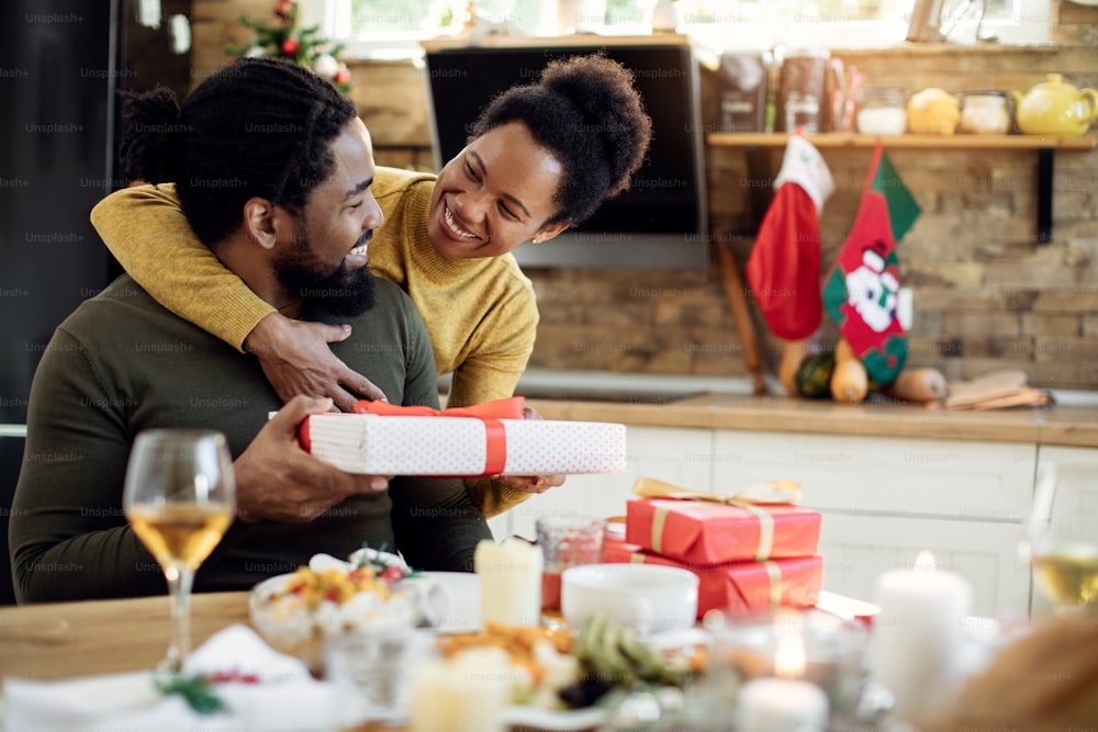 Happy African American woman surprising her husband with Christmas present.