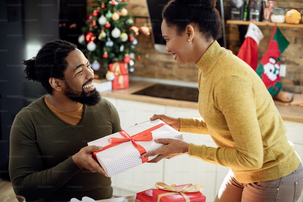 Happy African American couple giving each other present on Christmas day at home.