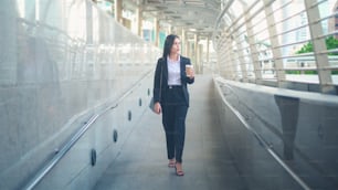 Une jeune femme d’affaires vêtue d’un costume noir utilise un téléphone intelligent, tenant une tasse de café dans la ville, Business Lifestyle Concept