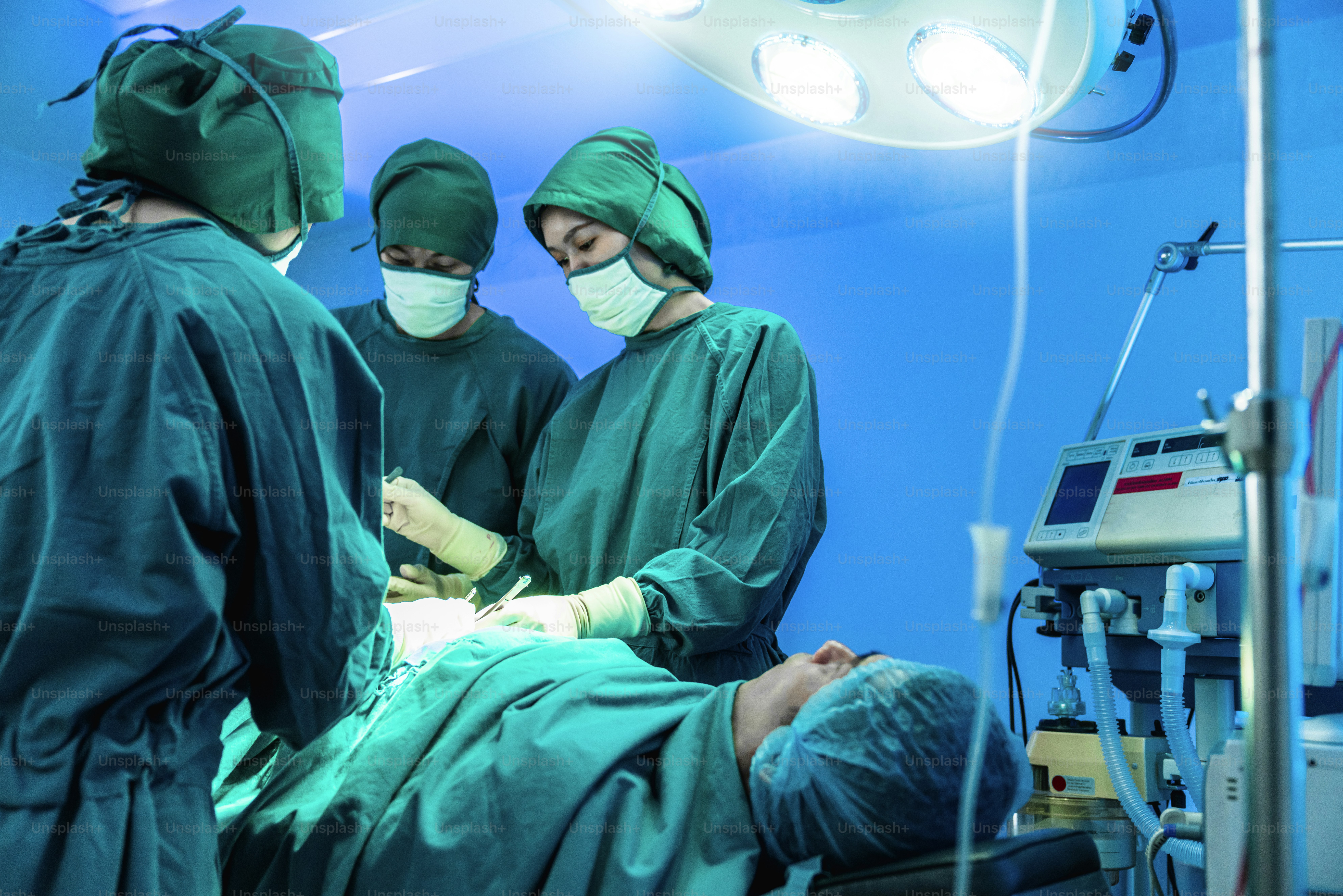 Three surgeons in green scrubs performing surgery on a patient in a bright room