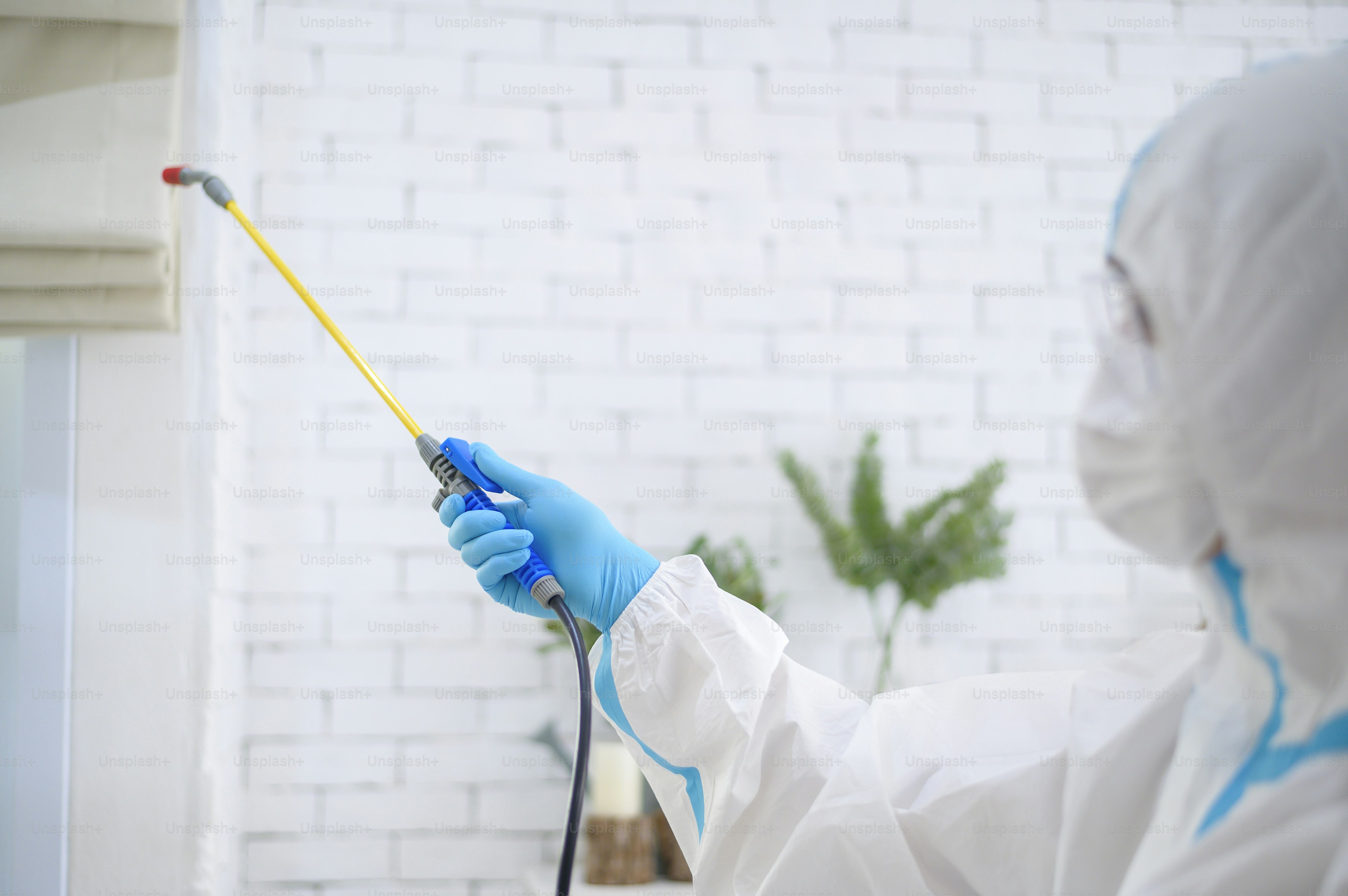 A medical staff in PPE suit is using disinfectant spray in living room, Covid-19 protection , disinfection concept .