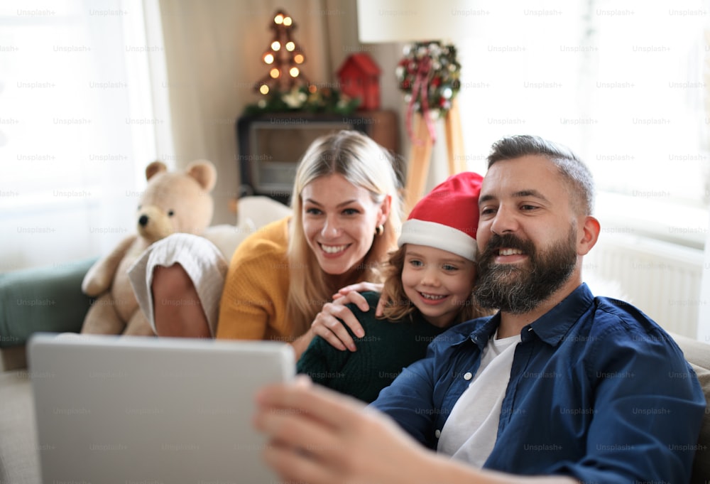 Famiglia con figlia piccola in casa a Natale, con videochiamata su tablet.
