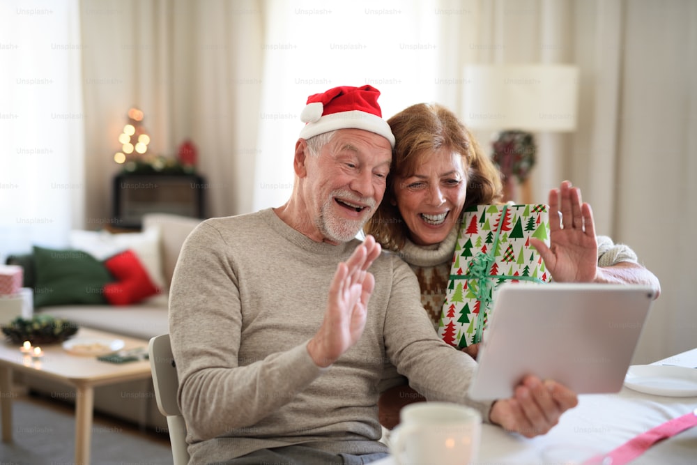 Front view of happy senior couple indoors at home at Christmas, having video call with family.