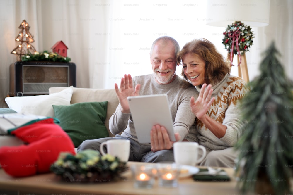 Vista frontal de una feliz pareja de ancianos en el interior de la casa en Navidad, teniendo una videollamada con la familia.