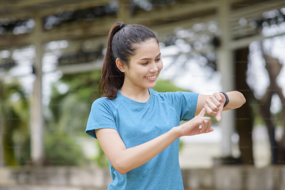 A happy young woman in sportswear using smart watch while exercising in park