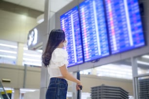 旅行者の女性が国際空港で防護マスクを着用している、Covid-19��パンデミック下での旅行、安全旅行、社会的距離のプロトコル、ニューノーマル旅行のコンセプト