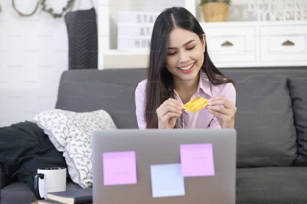 Una joven hermosa mujer está usando la tarjeta de crédito para las compras en línea en el sitio web de Internet en casa, concepto de comercio electrónico