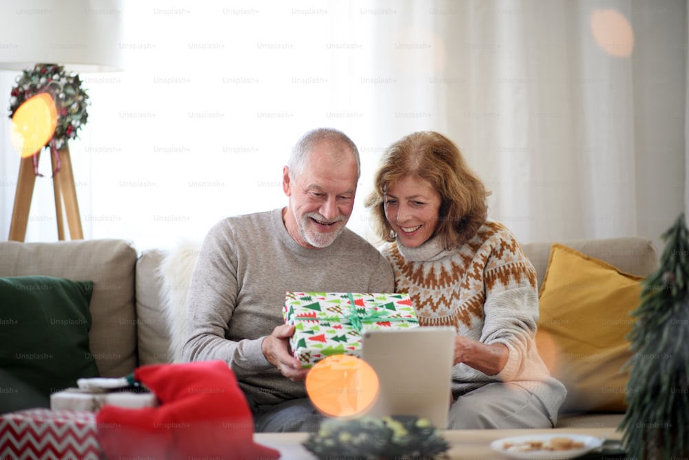 Vorderansicht eines glücklichen älteren Paares zu Weihnachten zu Hause, mit Videoanruf mit der Familie.