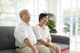 Elderly Asian couple watching television sitting on a sofa
 spending time together at home, retirement concept