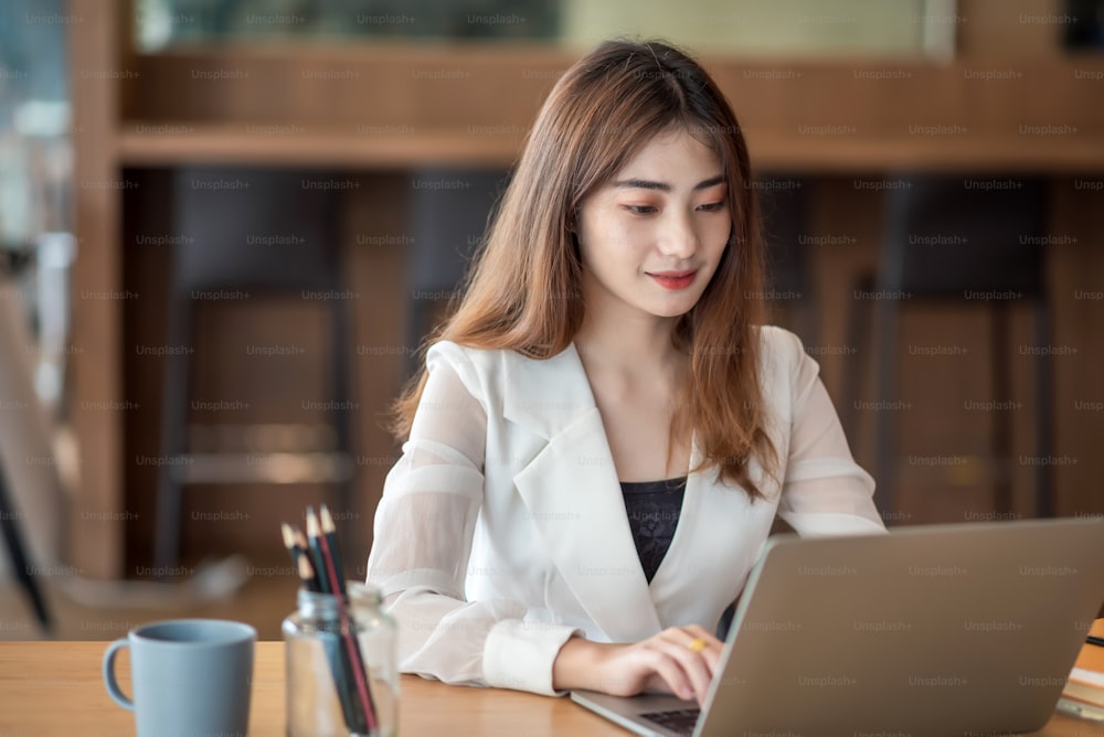 Joven mujer de negocios asiática hermosa, encantadora, sonriente y usando una computadora portátil en una oficina moderna.