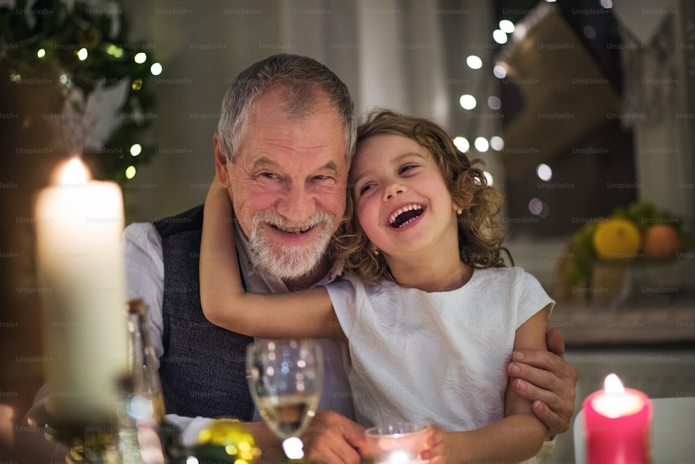크리스마스에 실내에서 작은 손녀와 함께 테이블에 앉아 있는 행복한 선배 할아버지.