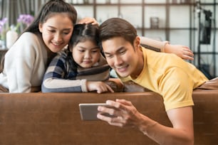 young happiness asian family hand selfie together with cheerful and fun due quarantine period new normal lifestyle,mom dad and daughter take photo selfie together on sofa in living room