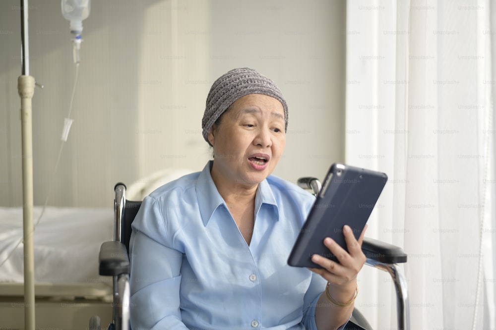 A cancer patient woman wearing head scarf making video call on social network with family and friends in hospital.