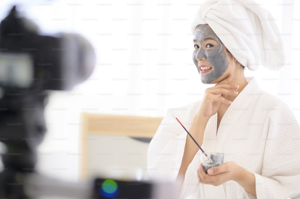 비디오 카메라 촬영 장면 뒤에서 영화를 위해 얼굴 마스크를 적용하는 흰색 목욕 가운을 입은 여자 촬영