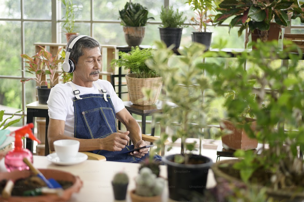 Ein glücklicher älterer asiatischer Rentner, der Musik hört und Freizeitaktivitäten im Garten zu Hause genießt.
