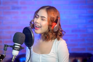 Une jeune chanteuse souriante portant des écouteurs avec un microphone tout en enregistrant une chanson dans un studio de musique avec des lumières colorées.