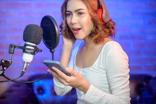 色とりどりの照明が光る音楽スタジオで、マイク付きのヘッドフォンを装着しながら曲を録音する若い笑顔の女性歌手。
