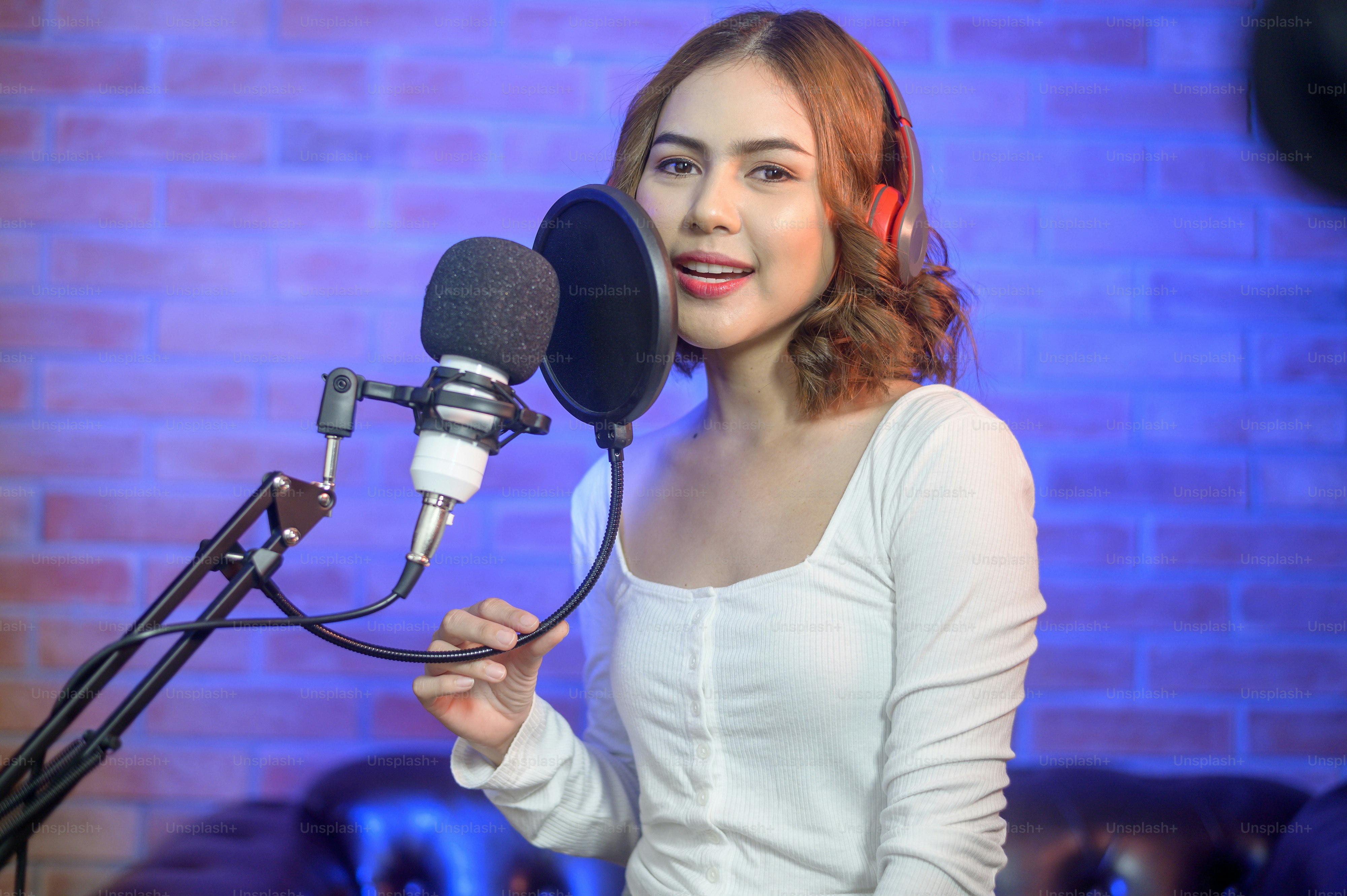 A young smiling female singer wearing headphones with a microphone ...