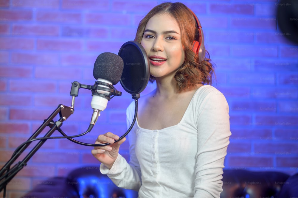 Une jeune chanteuse souriante portant des écouteurs avec un microphone tout en enregistrant une chanson dans un studio de musique avec des lumières colorées.