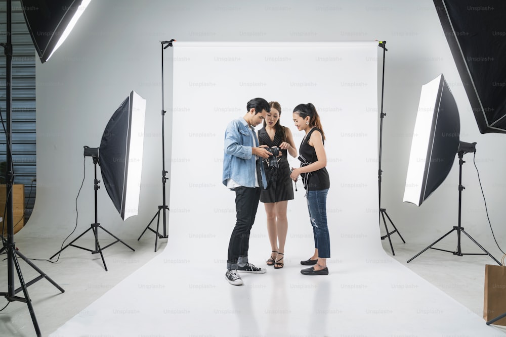 Hinter den Kulissen des professionellen Fotoshootings im Studio: Ein schönes junges asiatisches Model lächelt und posiert mit Visagistin ist Make-up-Fotograf fotografiert mit einer Digitalkamera