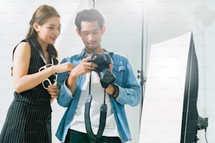 dietro le quinte del servizio fotografico professionale in studio: una bella giovane modella asiatica sorride e posa con il truccatore è il fotografo truccatore sta scattando foto con una fotocamera digitale