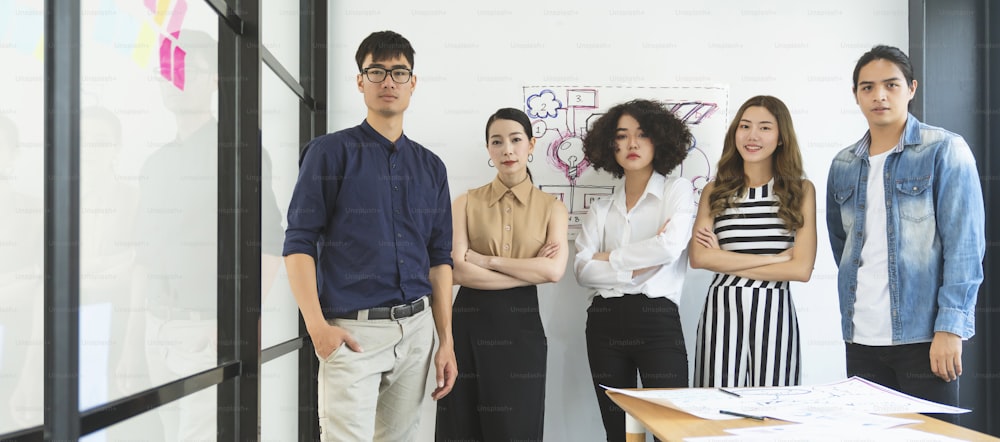Smart asian startup small entrepreneur  standing confident portrait with  friends partner casual meeting brainstorm with white board and business financce paper chart anslysis in office background