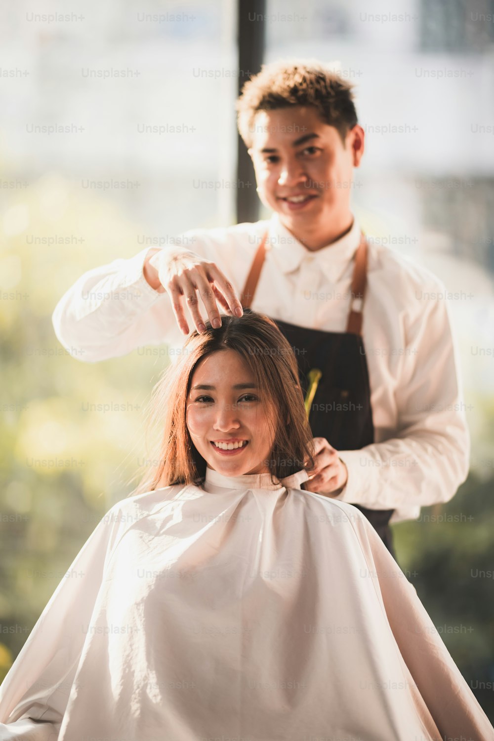 Professional hirdresser design the hair style of smilling young lady with bright brown colour and cutting at salon barber